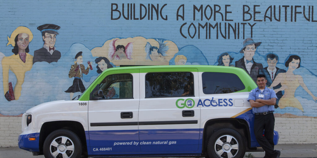 side view of paratransit vehicle in front of blue wall saying building a better community